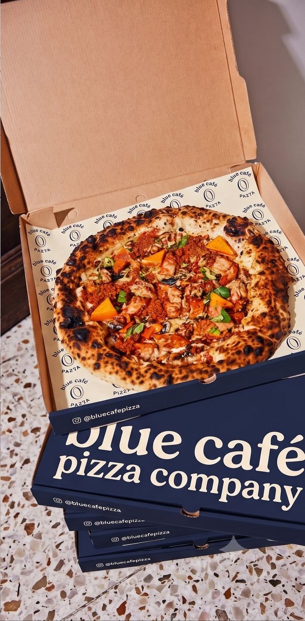 Open pizzadoos met pizza op Blue Café inpakpapier, op een stapel navy dozen
